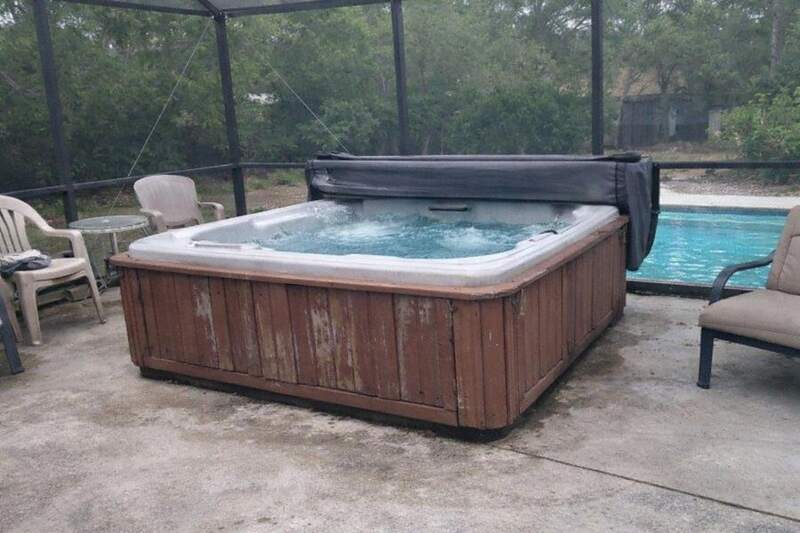 An old hot tub with a faded cabinet sitting inside a screened lanai in Florida