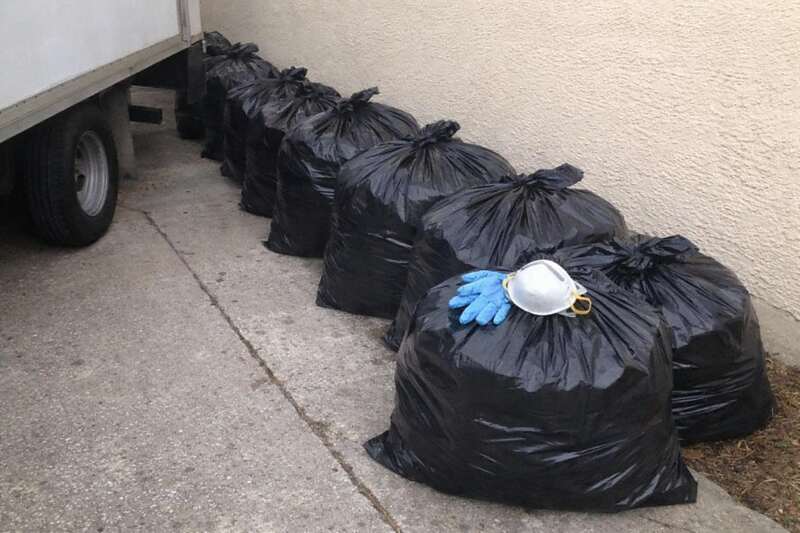 A row of tied contractor bags along a driveway with gloves and a dust mask on top