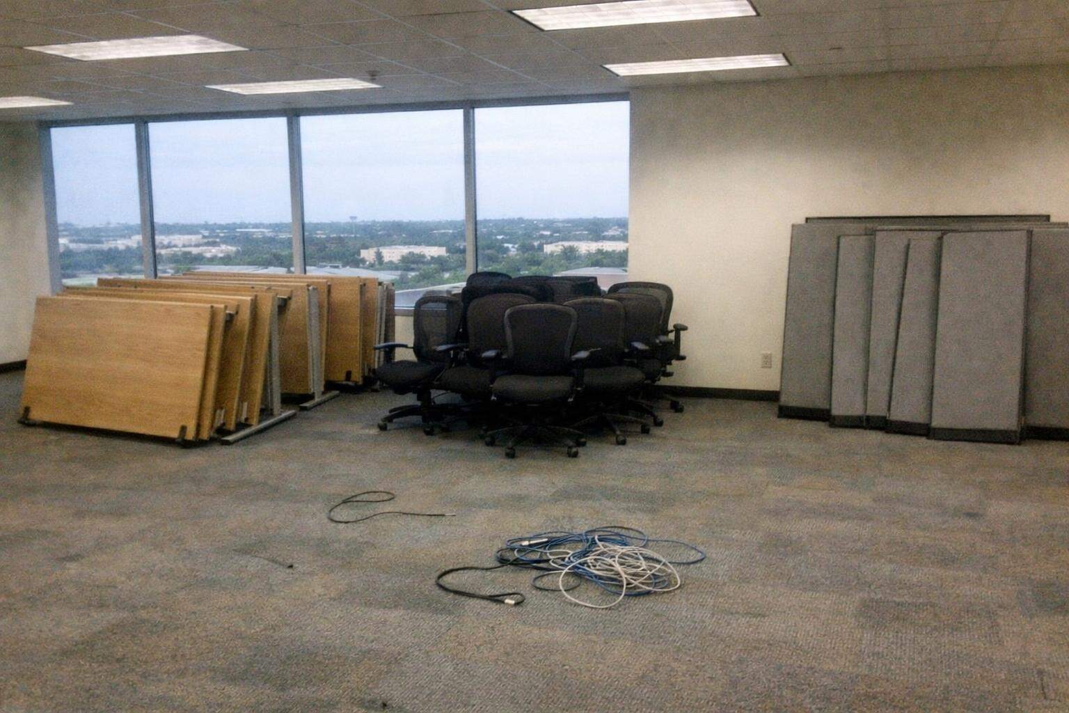 An empty office floor with desks stacked on their sides and cubicle panels leaning against the wall