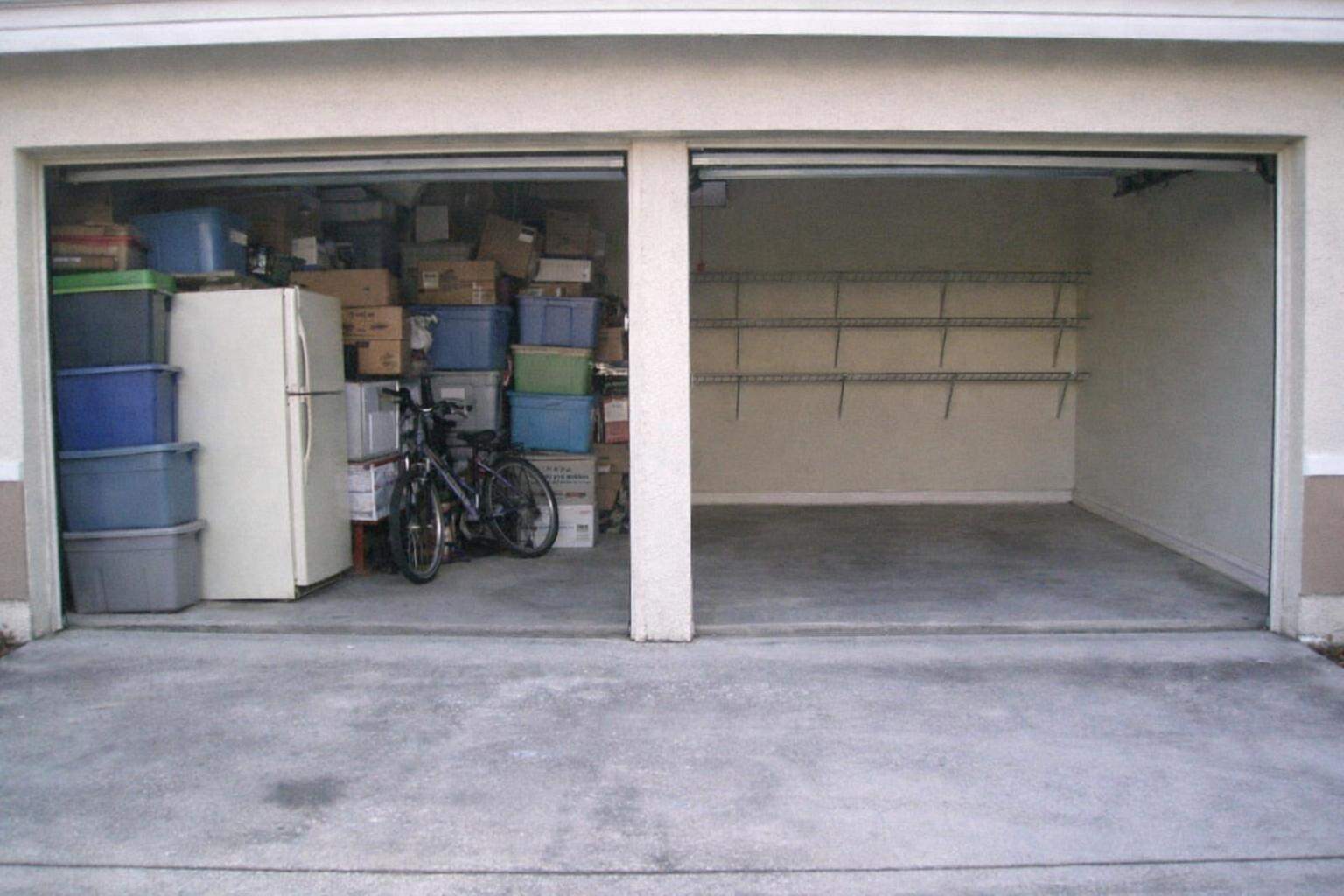 A two-car garage with one bay packed to the ceiling and the other swept clean