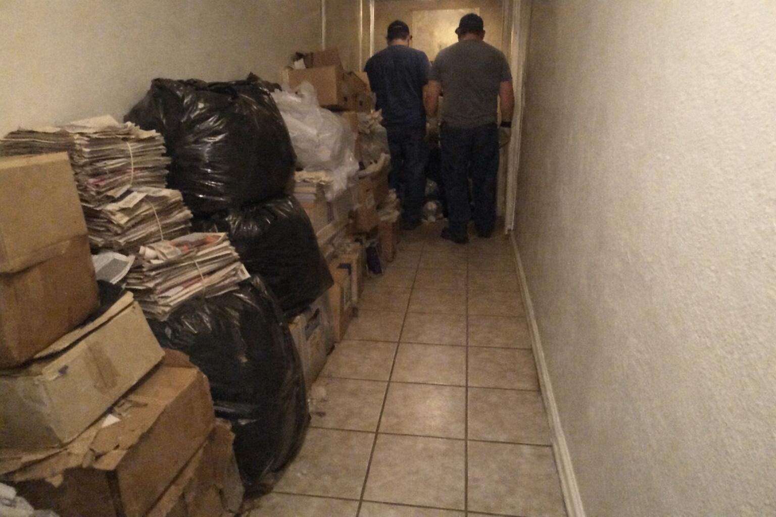A hallway half cleared, bagged refuse on one side and swept floor tile on the other